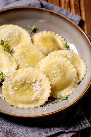 Fresh homemade ravioli pasta with parmesan cheese and thyme herbs served on ceramic plate. Traditional Italian cuisine dish.の写真素材