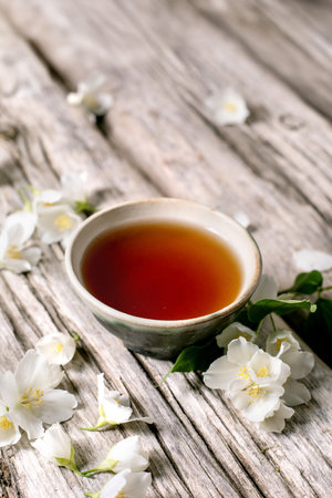 Cup of herbal tea with white jasmine flowers on rustic wooden table. Natural beverage scene with floral decoration.の写真素材