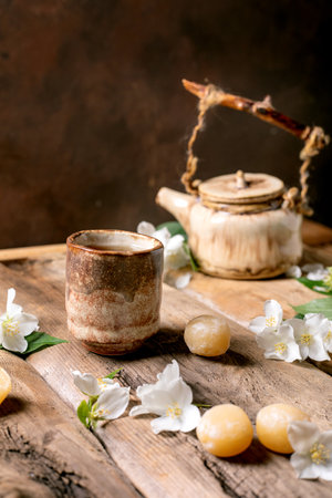 Ceramic teapot and cup on wooden table decorated with white jasmine flowers and traditional Japanese mochi sweets creating a peaceful tea ceremony atmosphereの写真素材