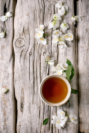 Cup jasmine tea with white flowers on rustic wooden background. Natural herbal drink with fresh blooms scattered around teacup on weathered wood surface.の写真素材