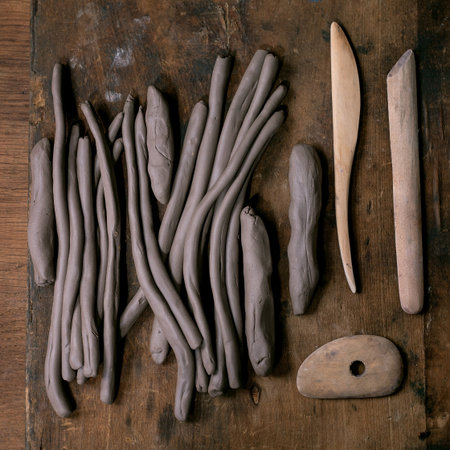 Pottery workshop preparation for children and adults: heap of raw clay ropes or sausages for work in coil technique, handmade spoons, pottery tools on a dark wooden table. Top viewの写真素材