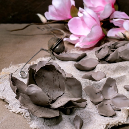 Creating Clay Flower: DIY ceramic Workshop Idea. Petals, buds prepared for crafting magnolia flower from dark clay on fabric. Dark textured background, ceramicist's tools, blooming magnolia. Top view.の写真素材
