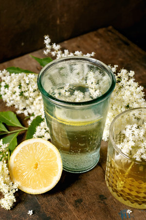 Refreshing elderflower beverage in glass with fresh lemon slice and white elderflower blossoms on wooden background. Natural herbal drink concept.の写真素材
