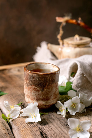 Ceramic tea cup with hot tea white spring flowers teapot on wooden table. Traditional oriental tea ceremony setup with natural decoration.の写真素材
