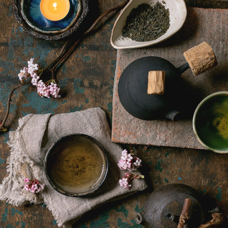 Chinese Tea Ceremony. Two traditional handmade ceramic black teapot with wooden handle on dark wooden table. Ceramic teacups and pink spring flowers, burning tea candle. Tea ceramics. Top view, spaceの写真素材