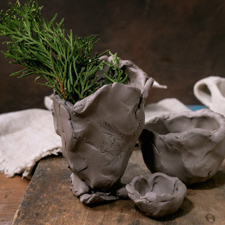 Ceramics workshop for children and beginners idea: vase and bowls made of raw clay, kids handmade decor. Dark wooden table.の写真素材