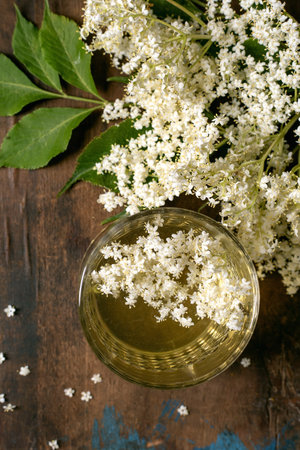 Glass cup elderflower tea with fresh white elderflower blossoms and green leaves on rustic wooden background top viewの写真素材