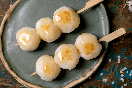 Traditional Japanese dango dumplings on bamboo skewers served on ceramic plate. Sweet glazed rice balls with golden caramelized coating authentic Asian dessert.の写真素材