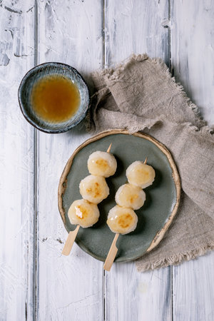 Top view Japanese dango dumplings on ceramic plate with tea bowl wooden sticks linen napkin on white...