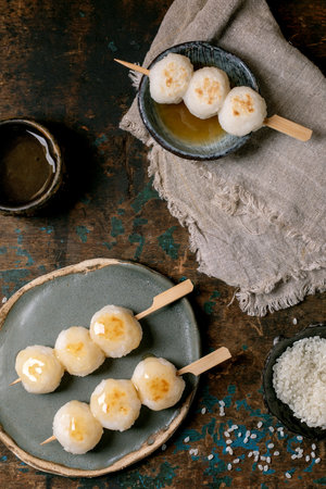 Traditional Japanese dango dumplings on skewers served on ceramic plates with tea. Sweet rice balls arranged on rustic wooden background with linen cloth.の写真素材
