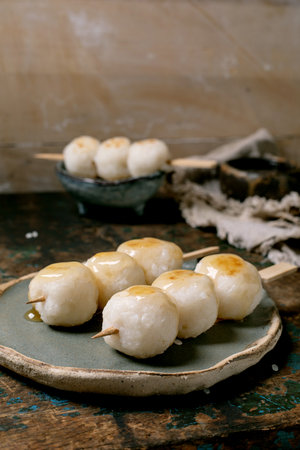 Traditional Japanese dango sweet rice dumplings on wooden skewers served on ceramic plate with rustic kitchen backgroundの写真素材