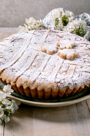 Delicious homemade shortcrust tart Pastiera Napolitano cake sprinkled with powdered sugar decorated with flower-shaped cookies on top white spring flowers background.の写真素材