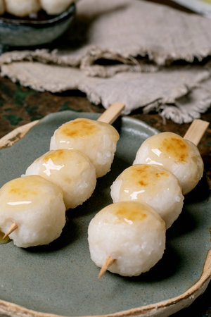 Traditional Japanese dango rice dumplings on wooden skewers served on ceramic plate. Sweet glazed mitarashi dango dessert with golden caramelized coating.の写真素材