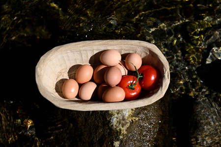 tomatoes and eggs in a basket on a wooden tableの写真素材