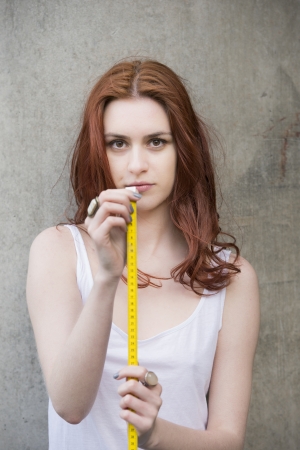 Young woman looking serious and holding measuring tapeの写真素材