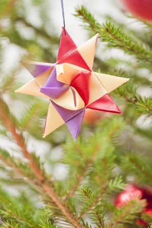 Decoration in shape of a colorful star hanging in a christmas treeの写真素材