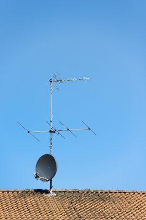 Aerial and satellite dish on roof of house with clear blue sky aboveの写真素材