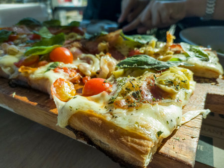 Pizza with ham, cheese, tomatoes and basil on a wooden boardの写真素材