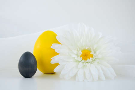 Large yellow and small gray egg and daisy flower on a white background with copy space. Happy easter concept, easter table, colors 2021 Ultimate Gray, Illuminating.の写真素材