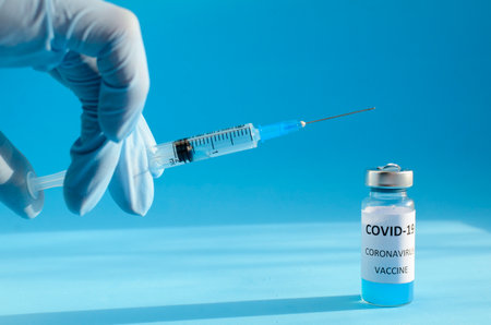 Hand in medical blue glove draws liquid into syringe for injection on blue background with copy...