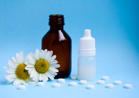 White medical tablets, chamomile, white and brown glass bottles on blue background with copy space. Concept of allergy treatment, medicines made from natural plant. Eye drops for allergies, rhinitis.の写真素材