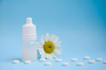 White medical tablets, chamomile, white bottle on blue background with copy space. Concept of...