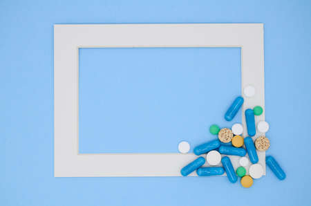 White frame and a lot of colorful medical pills, capsules on blue background with copy space.の写真素材