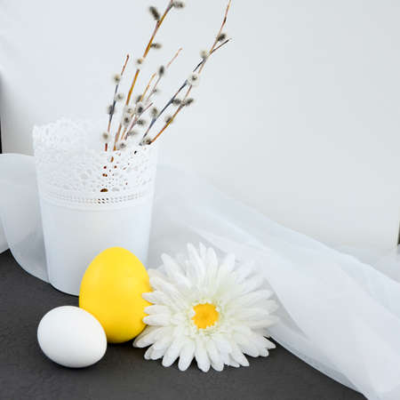 Large yellow and small white egg and daisy flower, willow branches in a white vase on gray background with copy space. Happy easter concept, easter table, colors 2021 Ultimate Gray, Illuminating.の写真素材