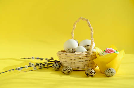 eggs in a white wicker basket and pussy willow branches, quail eggs, easter cake on yellow...