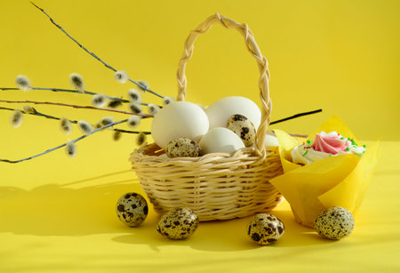 eggs in a white wicker basket and pussy willow branches, quail eggs, easter cake on yellow background with copy space. Happy Easter concept, Easter table.の写真素材