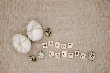 Two wooden eggs with twine bows, quail eggs on burlap background with copy space. Inscription happy...