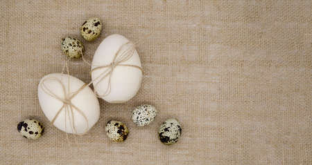 Two wooden eggs with twine bows, quail eggs on a burlap background with copy space. Concept of Happy Easter.の写真素材