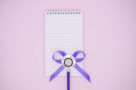 Stethoscope, Notepad and bow of purple ribbon on pink background with copy space. Medical flat lay.の写真素材