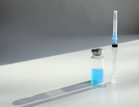 Glass bottle with blue liquid and syringe on gray background with copy space and shadows. Concept of vaccinationの写真素材