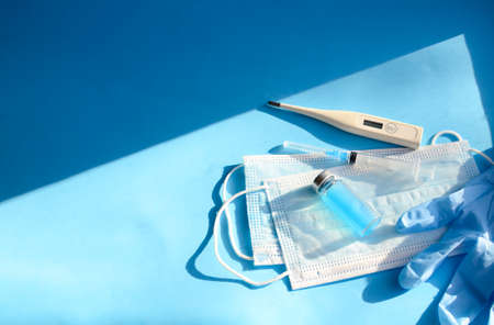 Glass bottle, medical masks, gloves, thermometer and syringe on blue background with copy space and...