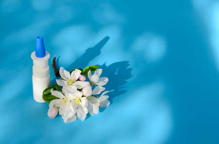 White dropper bottle and spring flowers on blue background with shadows with copy space. Concept of allergy treatment. Nose drops ore spray for allergies, rhinitis.の写真素材