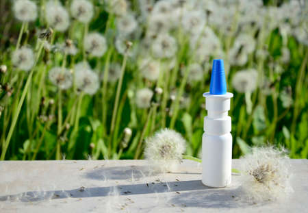 White dropper bottle and spring flowers on gray background with shadows with copy space. Concept of allergy treatment. Nose drops ore spray for allergies, pollinosis, rhinitis.の写真素材