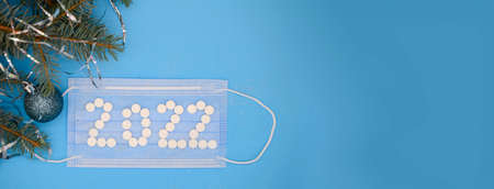 White medical pills in the form of the number 2022 on a medical face mask and a Christmas tree with a Christmas glitter ball on a blue background. Christmas medical flatly.の写真素材