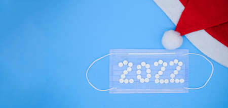 White medical pills in form of the number 2022 on a medical face mask and Santa hat on a blue background. Christmas medical flatly.の写真素材