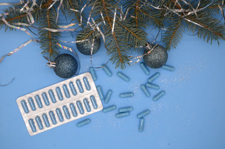 Blue medical capsules and blister with blue capsules and a Christmas tree with a Christmas glitter balls on a blue background with copy space. Christmas medical flat.の写真素材
