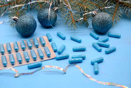 Blue medical capsules and blister with blue capsules and a Christmas tree with a Christmas glitter balls on a blue background. Christmas medical flatly.の写真素材