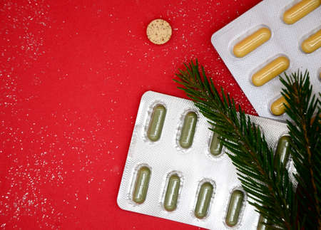Top view of Christmas tree and yellow and green medical capsules in a blister, medical pills on a red background. Medical Christmas concept.の写真素材