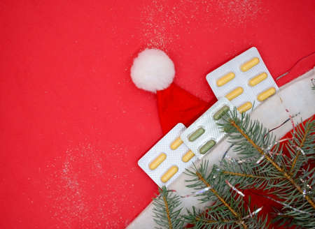 Top view of yellow and green medical capsules in a blister, medical pills in a Santa hat on a red background. Medical Christmas concept.の写真素材