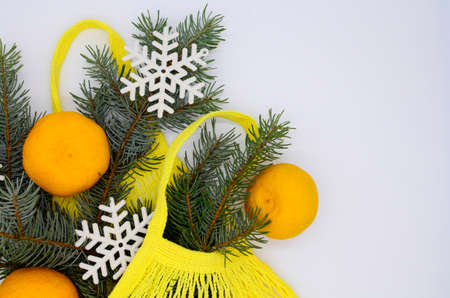 Three clementines in yellow eco string shopping bag with Christmas tree and snowflakes on white background with copying space. Christmas flat lay. Christmas shopping concept.の写真素材