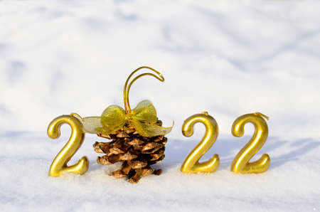 Number 2022 gold color and a cone with a golden bow in the snow with copy space. Concept of...