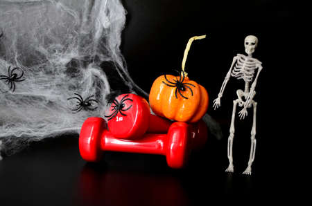 Two red dumbbells, skeleton, pumpkin, spider web on black background with copy space. Concept of Halloween, sports.の写真素材