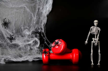 Two red dumbbells, skeleton, spider web on black background with copy space. Concept of Halloween, sports.の写真素材