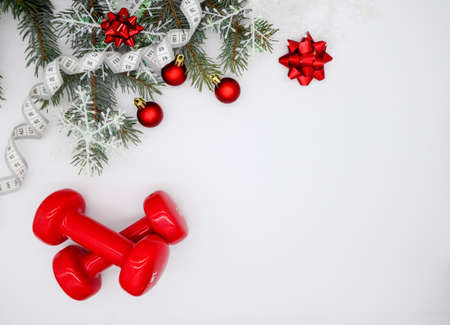 Two red sports dumbbells and a Christmas tree with snowflakes and red balls, white measuring tape on a white background with copy space. Christmas sport flatly. Concept of a healthy lifestyle.の写真素材