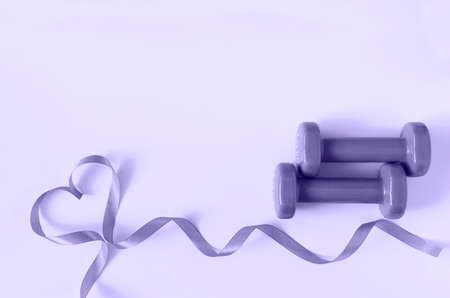 Two dumbbells with heart from ribbon in color of year 2022 Very peri with copy space. Concept of Valentines day, love, healthy lifestyle, giving gifts, love of sports.の写真素材
