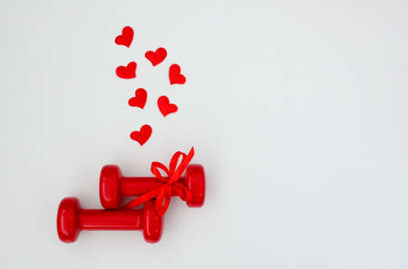 Two red dumbbells and hearts on a white background with copy space. Concept of Valentines day, healthy lifestyle, giving gifts, love of sports, shoppingの写真素材